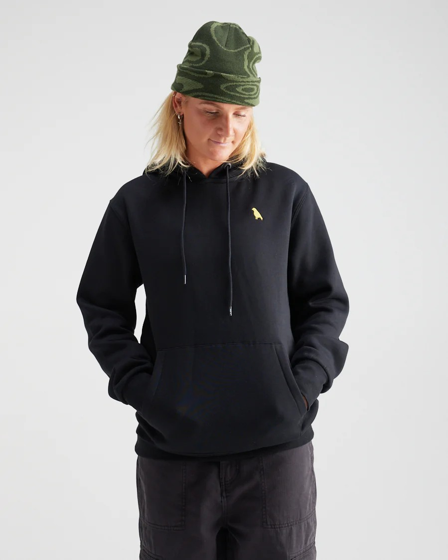 Person wearing a black hoodie with a small yellow logo and a green beanie on a light gray background